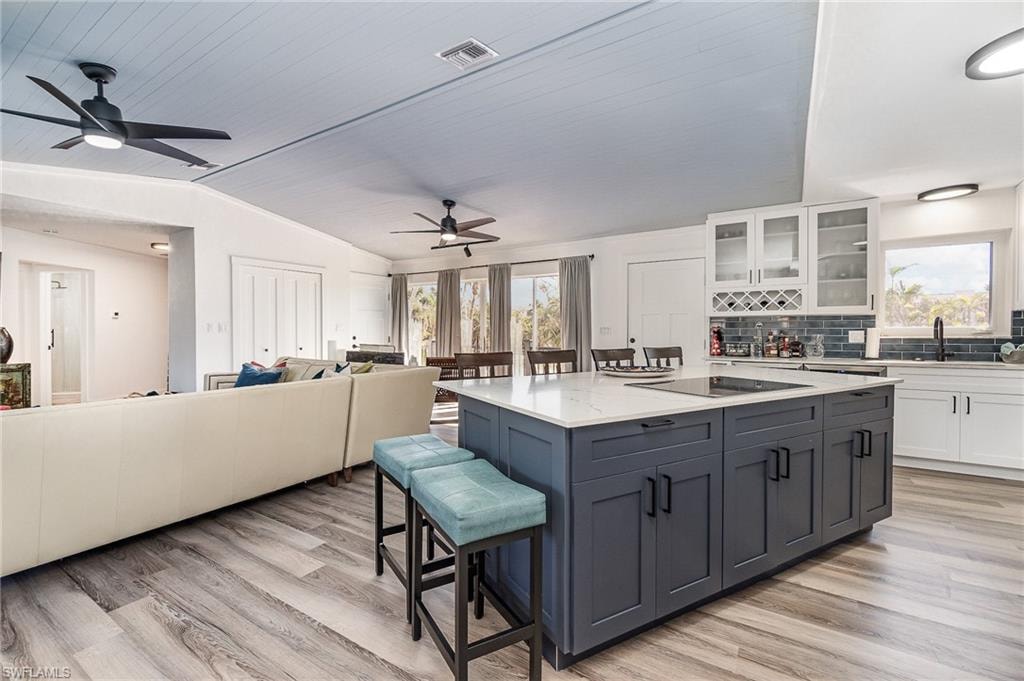 Kitchen featuring a central island with integrated cooktop, white perimeter cabinetry, dark subway tile backsplash, and wood-finish flooring