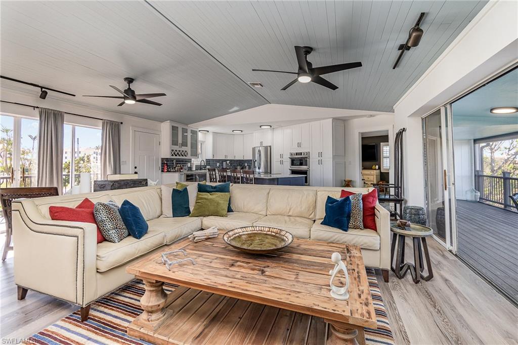 Open-concept living area featuring light wood-finish flooring, a light blue beadboard ceiling with twin ceiling fans, and sliding glass doors opening to an outdoor deck