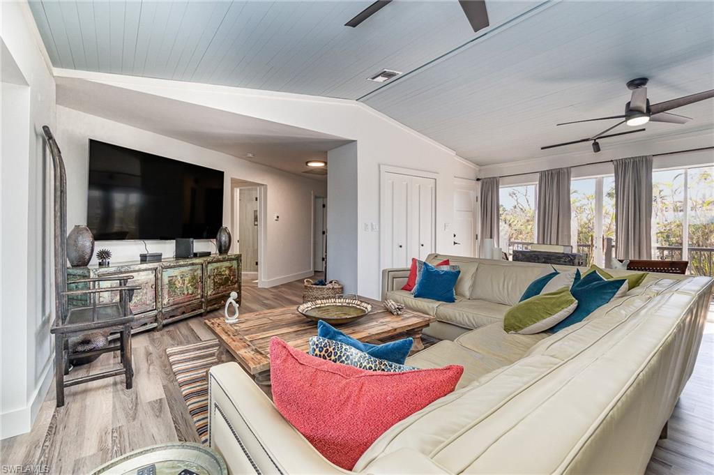 Spacious living area featuring wood-finish flooring, a vaulted plank ceiling, and multiple ceiling fans