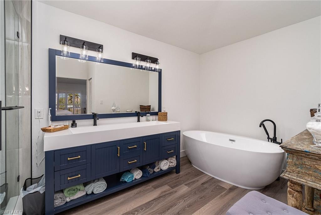 Bathroom with wood-finish flooring, a freestanding soaking tub, and a dual vanity featuring a white countertop and navy cabinetry with gold-tone hardware