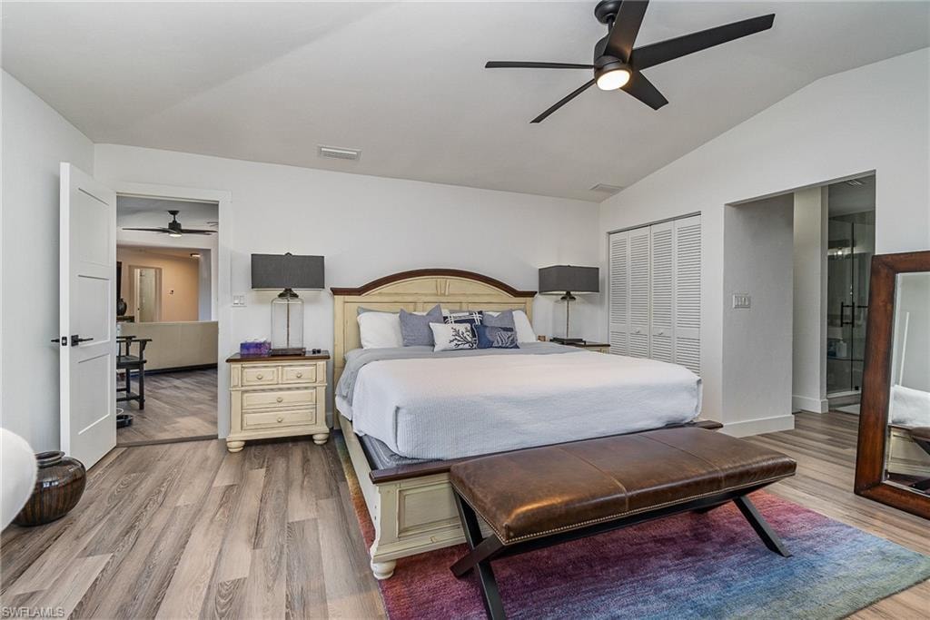 Spacious bedroom featuring vaulted ceilings, wood-finish flooring, a contemporary ceiling fan, and louvered bifold closet doors