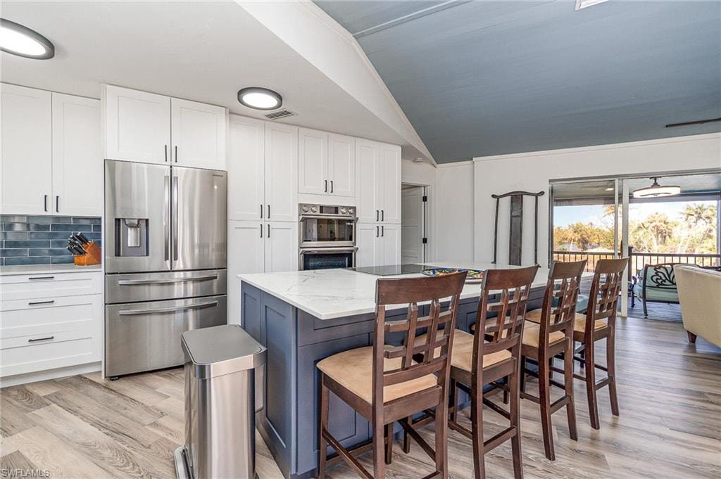 Modern kitchen featuring white shaker cabinetry, stainless steel appliances, a blue tile backsplash, and a central island with countertop seating
