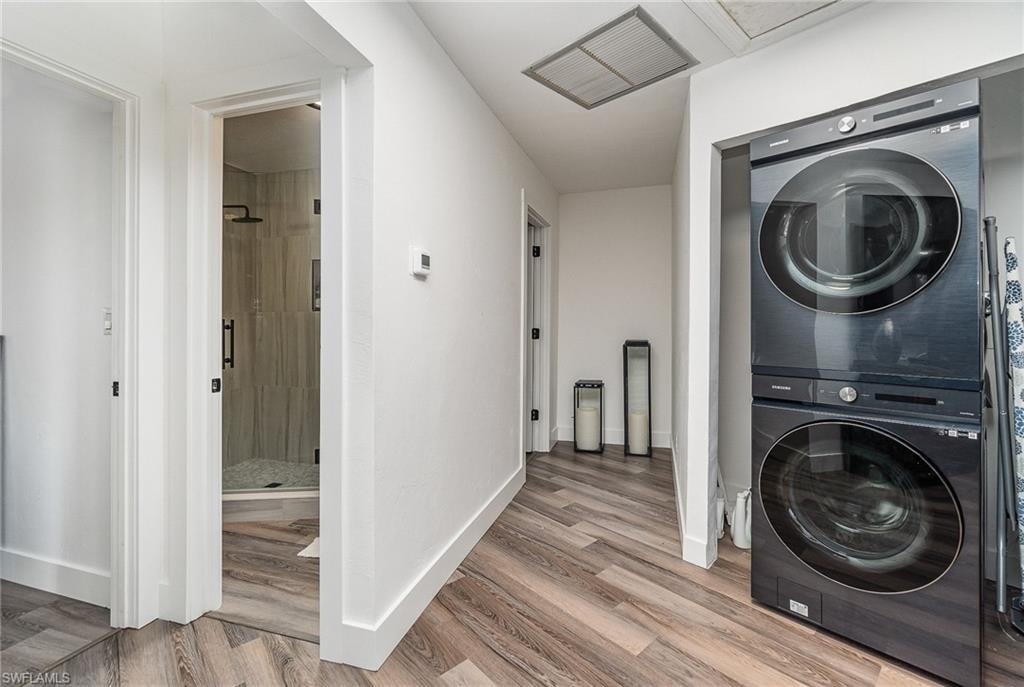 Hallway featuring wood-finish flooring, a stacked washer and dryer unit, and a doorway leading to a bathroom with a glass-enclosed shower