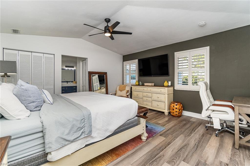 Vaulted ceilings with a ceiling fan, plank-style flooring, white louvered bifold closet doors, and plantation shutters