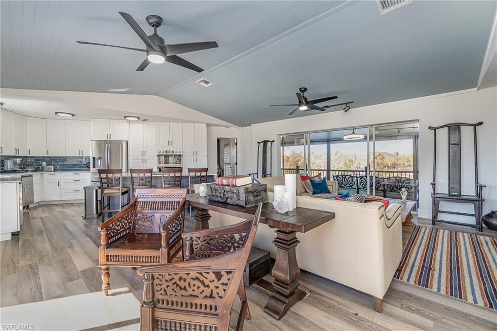 Open-concept living space with wood-finish flooring, a kitchen featuring white cabinetry and stainless steel appliances, and a screened patio with decorative railing