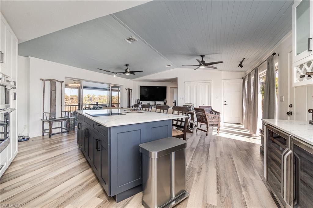 Kitchen featuring a substantial island with quartz countertops and a built-in sink, light wood-finish flooring, white cabinetry with dark hardware, recessed lighting, and a paneled ceiling with a light blue finish