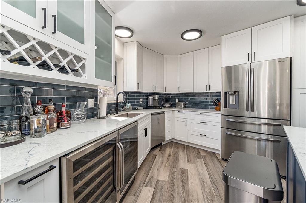 Modern kitchen featuring white shaker cabinetry with matte black hardware, stone countertops, a blue subway tile backsplash, stainless steel appliances, and wood-finish flooring