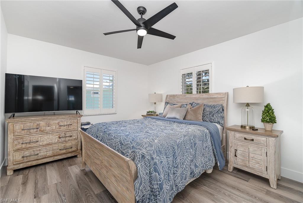 Spacious room featuring wood-finish flooring, white walls, and a black ceiling fan with integrated lighting