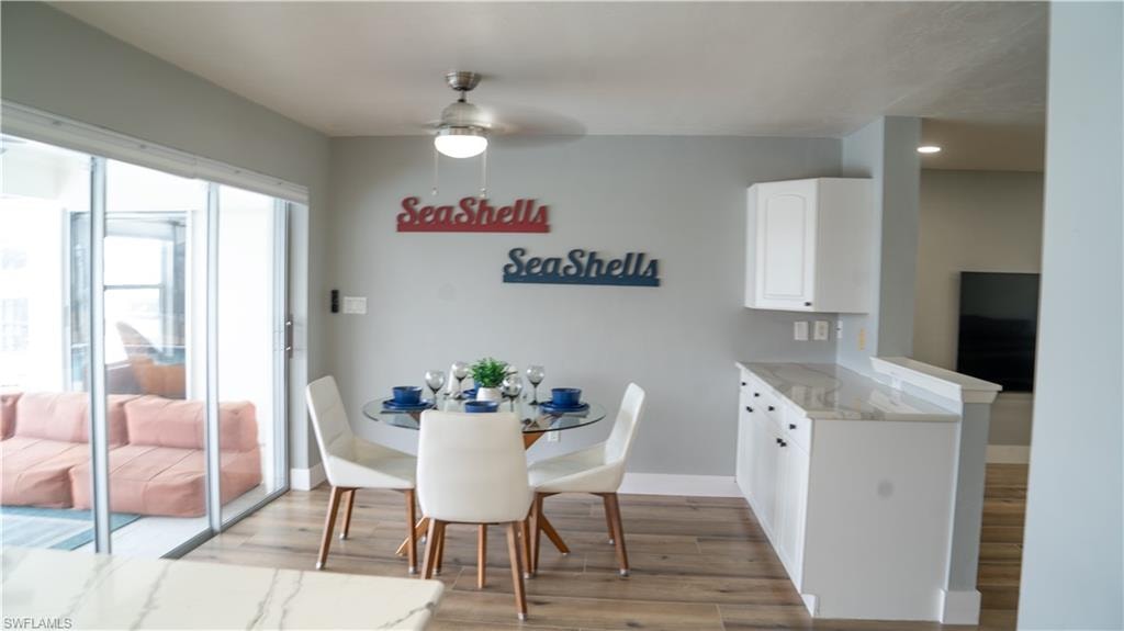 Sliding glass doors opening to an outdoor area with seating, wood-finish flooring, a ceiling fan with light fixture, and white cabinetry with a light-toned countertop