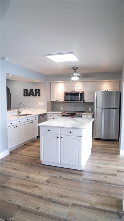 Kitchen featuring white shaker cabinetry, stainless steel appliances, a central island with countertop, wood-finish flooring, and a subway tile backsplash