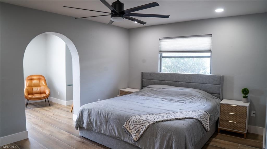 Bedroom featuring an arched doorway, wood-finish flooring, a contemporary ceiling fan, recessed lighting, and a window with a cellular shade