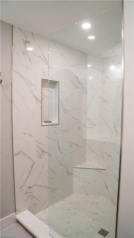Glass-enclosed shower featuring white and gray veined tile walls