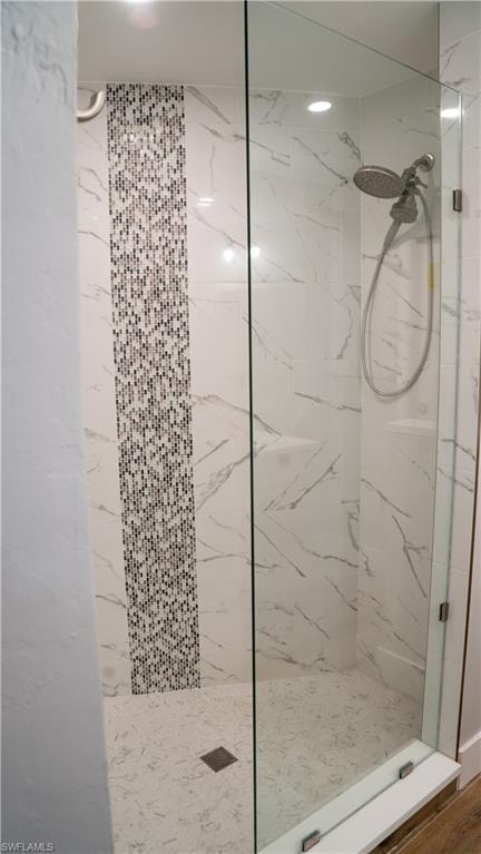 Walk-in shower featuring a frameless glass enclosure, large format white marble-look wall tiles, and a mosaic tile accent strip