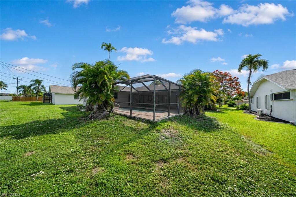 Screened pool enclosure with a paved deck, surrounded by verdant lawn and mature palm trees