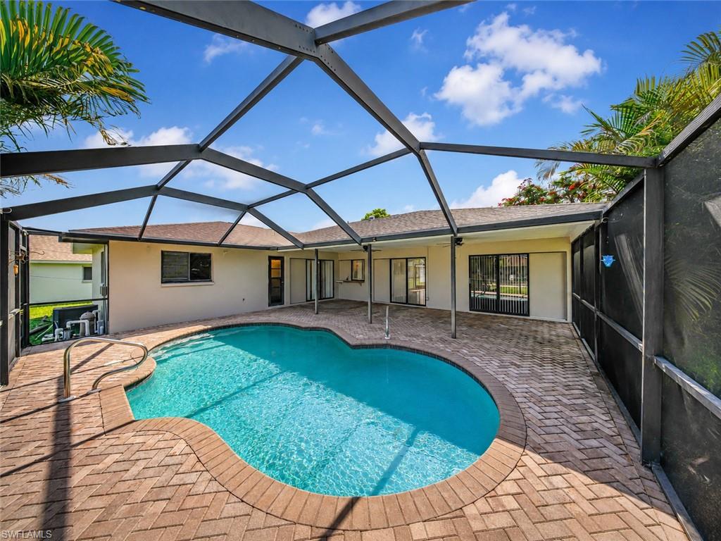 Screen-enclosed pool area featuring a freeform swimming pool, brick paver patio, and multiple glass sliding doors providing access to the interior