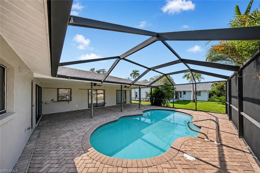 Screened-in pool deck featuring a freeform swimming pool, brick paver patio, and multiple access points to the residence