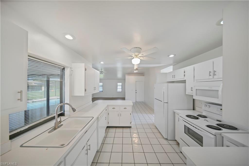 Bright kitchen featuring white cabinetry, a dual-basin sink with a gooseneck faucet, white appliances, recessed lighting, and a ceiling fan