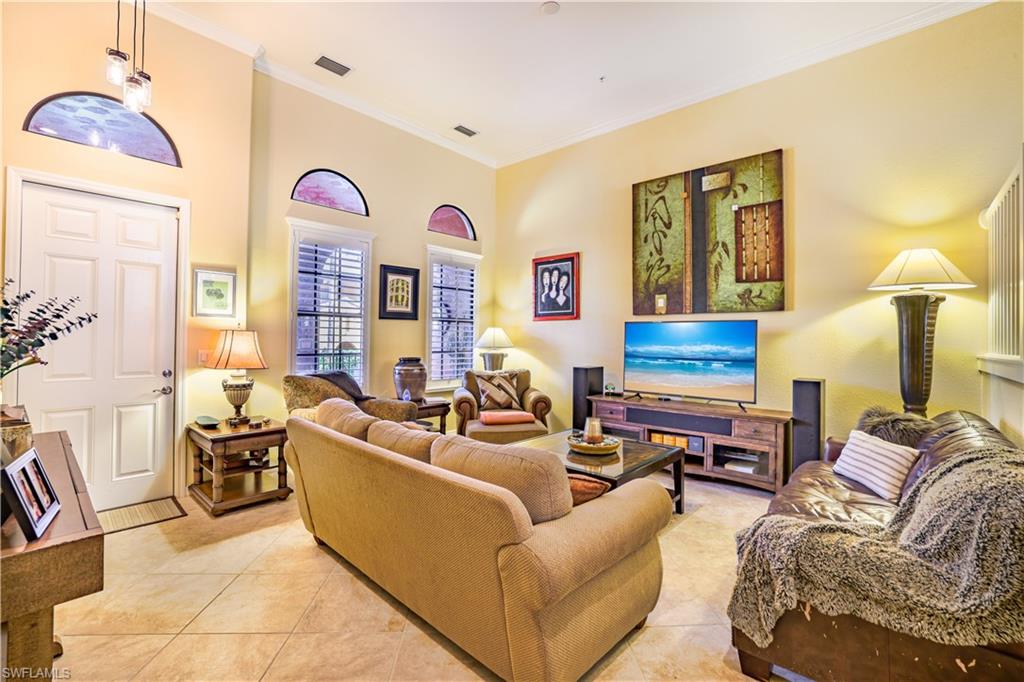 Spacious living area featuring high ceilings, tile flooring, arched transom windows, a paneled entry door, and vertical window blinds