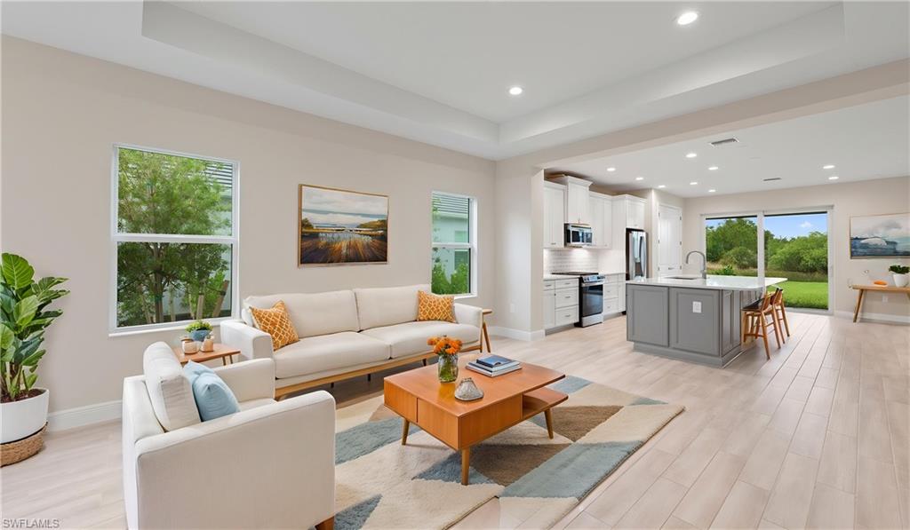 Open-concept great room with a recessed tray ceiling, recessed lighting, and Whitewash wood-look plank tile flowing into the kitchen and dining, framed by impact-glass windows that fill the space with natural light.