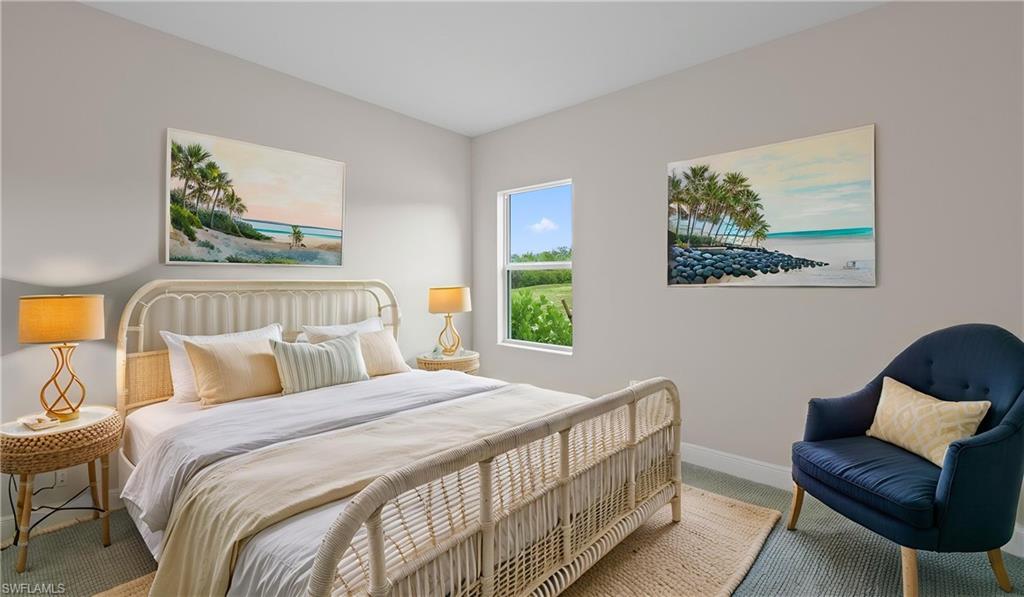 A serene guest bedroom with plush patterned carpeting, beach-inspired artwork, a cozy accent chair, and bright light from an impact-glass window.