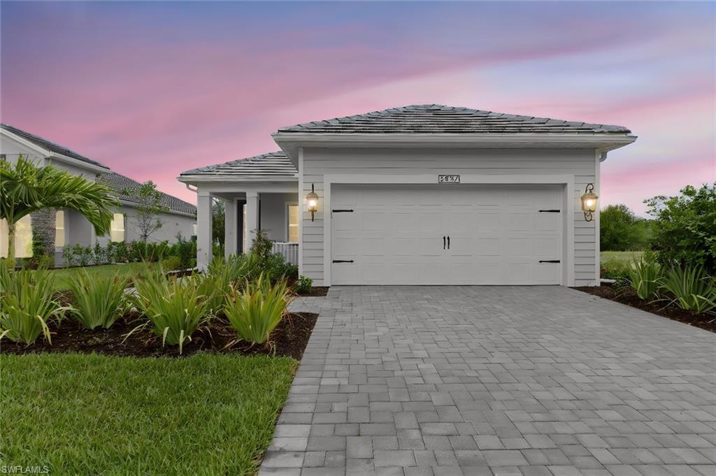 Coastal-elevation curb appeal with a Slate paver driveway, extended two-car garage, and black coach lighting beneath a concrete tile roof, built with whole-house hurricane impact glass in the gated Verandah golf community.