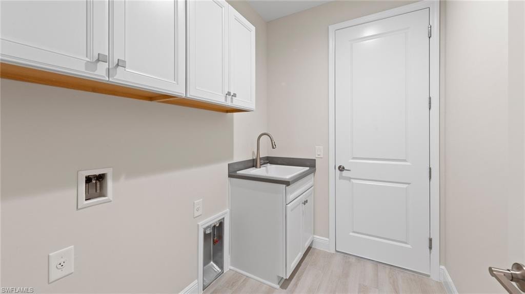 A functional laundry room with white Wentworth cabinetry, a Corian-topped utility sink, wood-look tile flooring, and washer/dryer hookups.