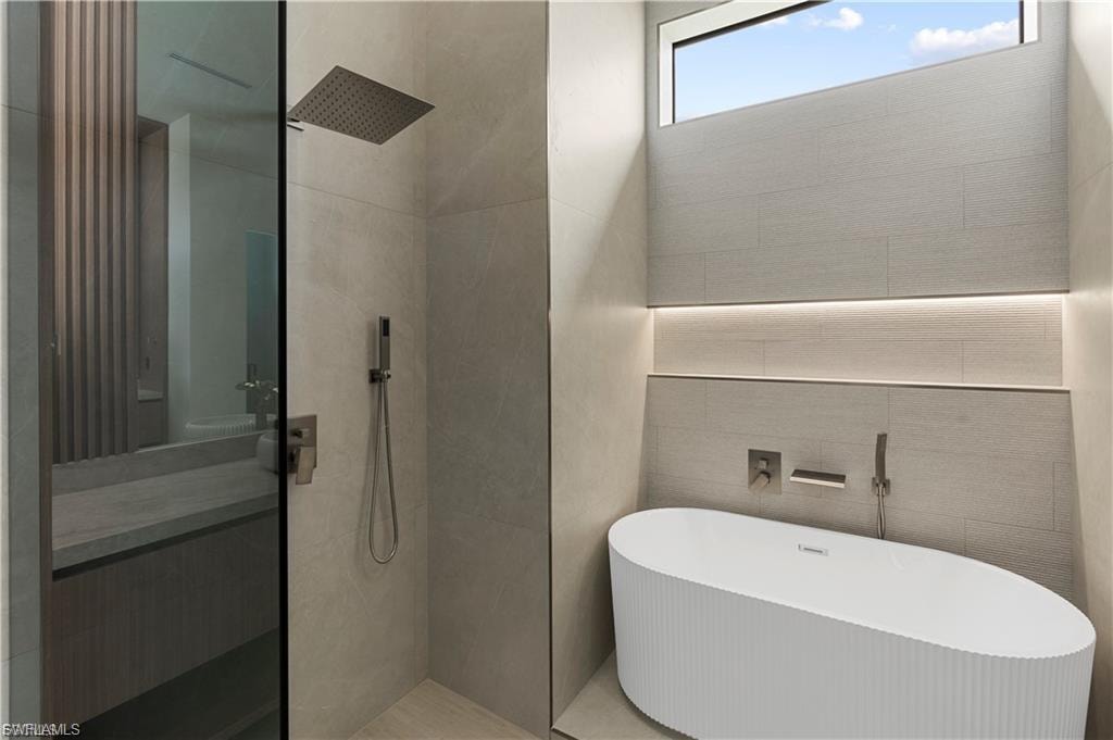 Contemporary bathroom featuring a freestanding soaking tub, a rain showerhead, a shower with a handheld sprayer, an integrated tiled shelf with subtle lighting, and a transom window