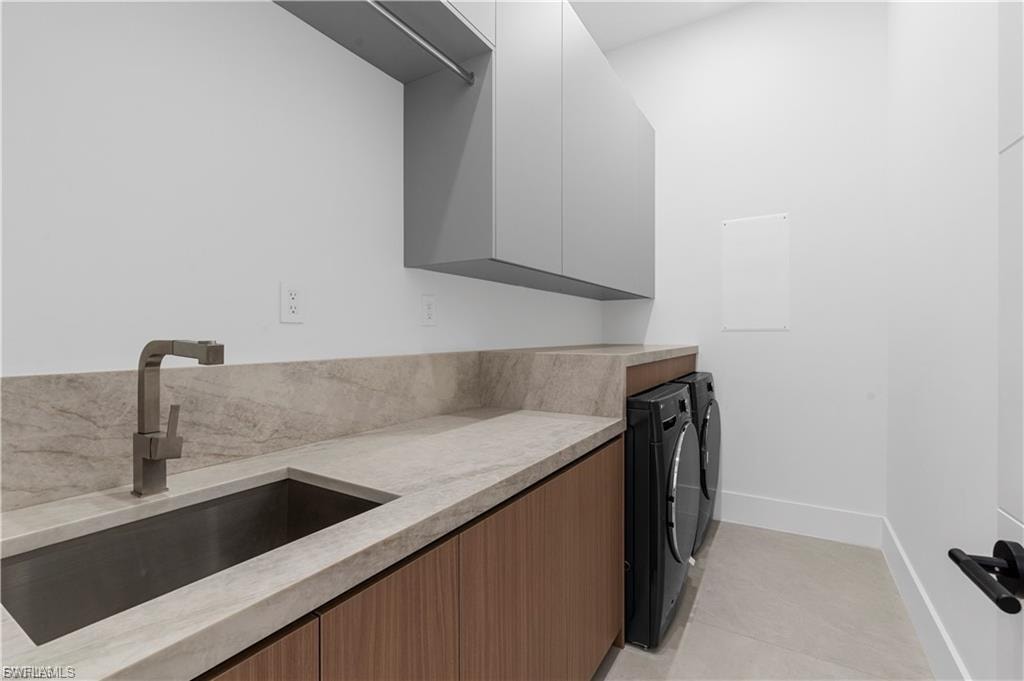 Contemporary laundry area featuring an integrated sink, matte black faucet, wood-finish cabinetry, light-toned countertops with a matching backsplash, and gray upper cabinetry