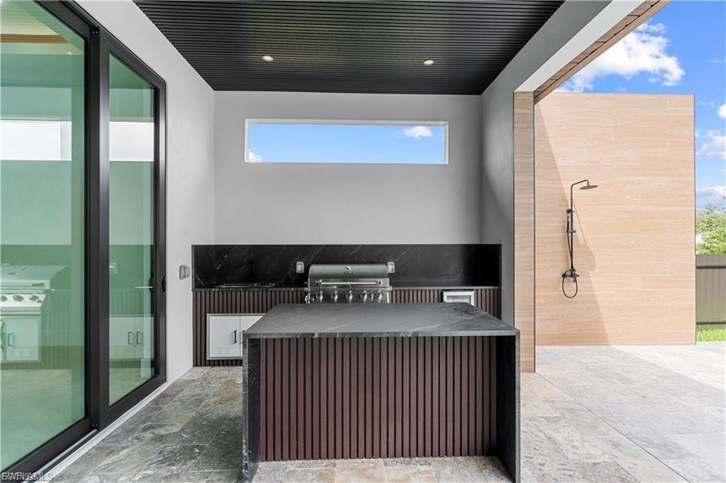 Outdoor entertaining area featuring a built-in grill, black stone countertops, and a waterfall-edge island with fluted wood-finish paneling