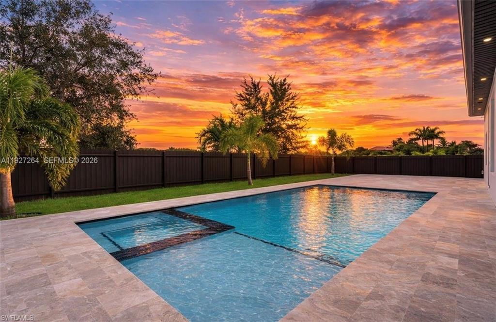 Expansive backyard featuring a rectangular swimming pool with an integrated spa, surrounded by large format stone-finish patio tiles