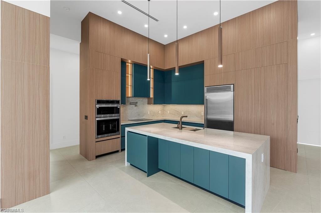 Contemporary kitchen featuring teal-finished cabinetry, integrated stainless steel appliances, a center island with a light-toned countertop, and wood-finish paneling