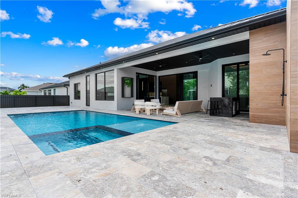 Resort-style patio featuring a rectangular swimming pool with integrated spa, expansive stone tile decking, a covered lanai with recessed lighting, and an outdoor shower with a wood-finish privacy wall