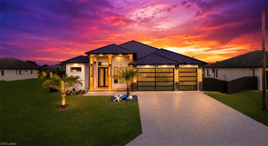 Contemporary architecture featuring a dark metal roof, clean white exterior, two-car garage with frosted glass doors, a paver driveway, and a manicured lawn with palm trees