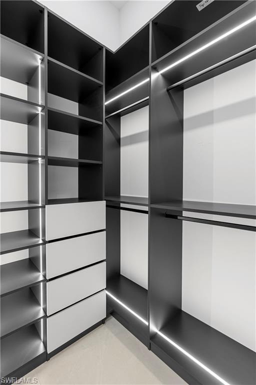 Custom closet system featuring dark cabinetry with integrated linear lighting, multiple shelving units, four white drawers, and hanging rods