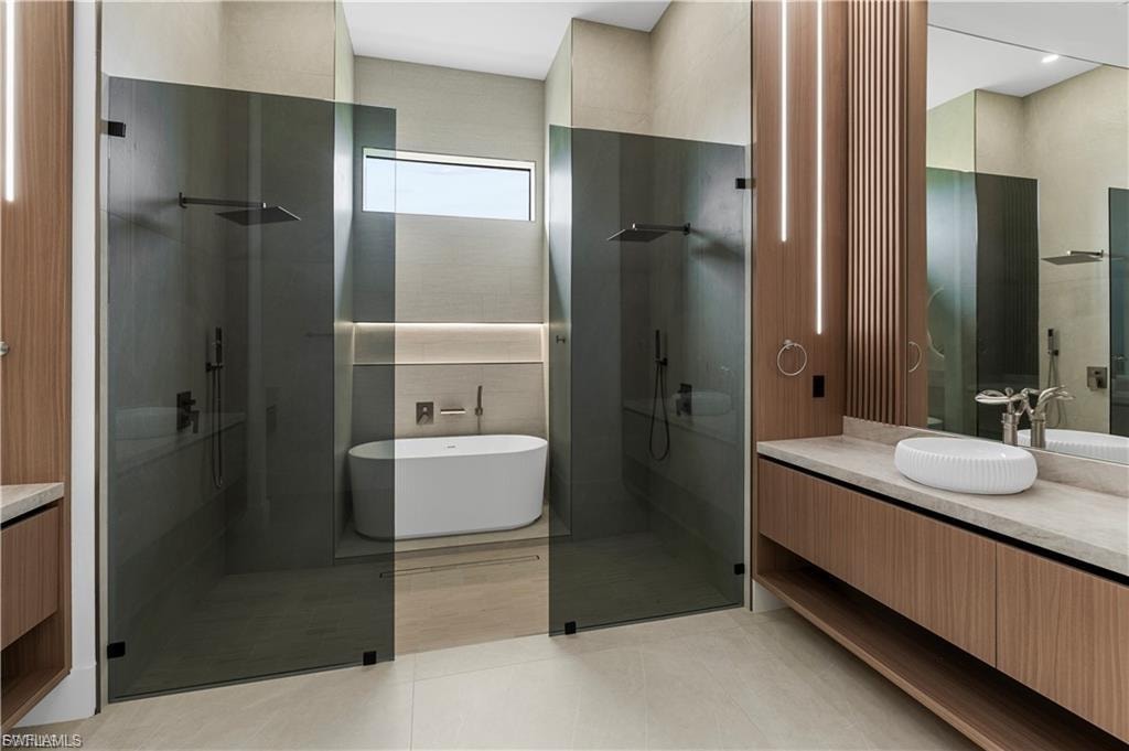 Contemporary bathroom featuring a freestanding tub, twin frameless glass shower enclosures with rainfall showerheads, and a floating wood-finish vanity with an integrated vessel sink