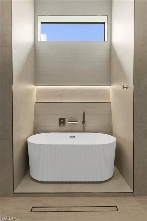 Freestanding soaking tub set within a tiled alcove featuring an integrated linear drain