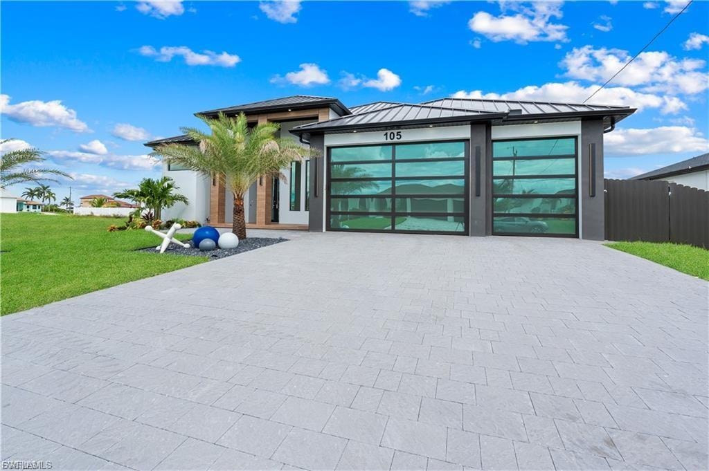 Contemporary exterior featuring a paver driveway, manicured lawn, and glass garage doors