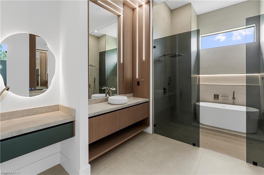 Modern bathroom featuring a freestanding tub, glass-enclosed shower, wood-finish vanity with vessel sink, and an illuminated mirror