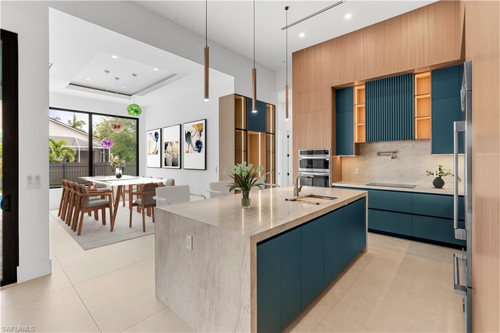 Modern kitchen featuring teal cabinetry, integrated stainless steel appliances, a large center island with a sink, and pendant lighting