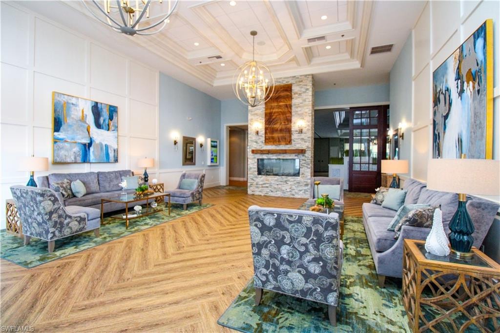 Living room with light parquet floors, coffered ceiling, a stone fireplace, a chandelier, and a high ceiling