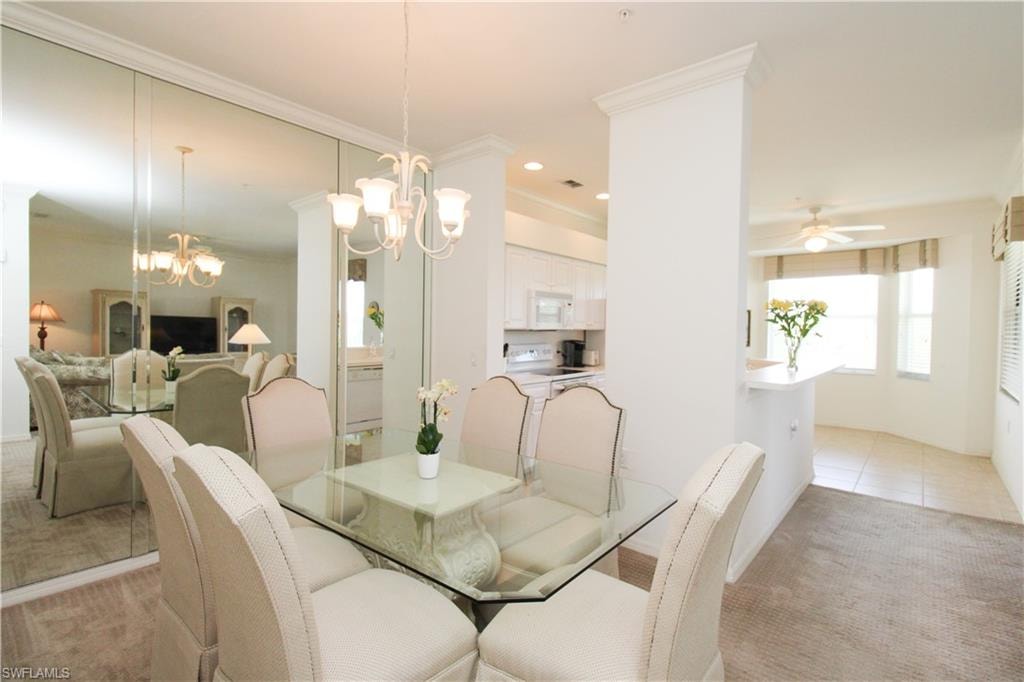 Carpeted dining room featuring ceiling fan with notable chandelier and crown molding
