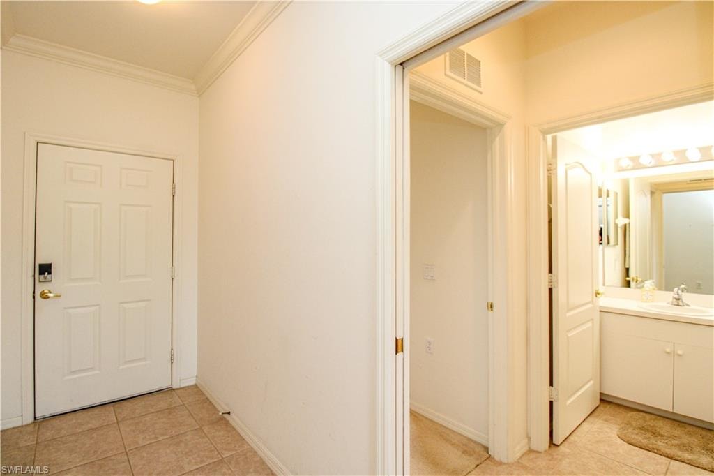 Corridor featuring sink, crown molding, and light tile patterned flooring