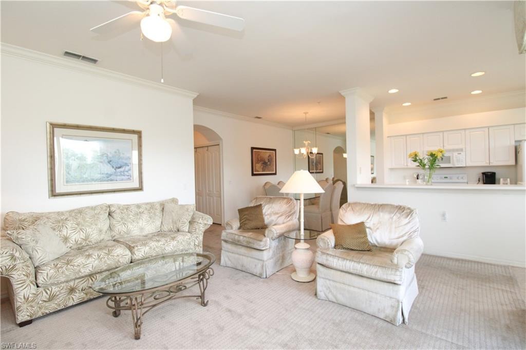 Carpeted living room with ornamental molding and ceiling fan with notable chandelier