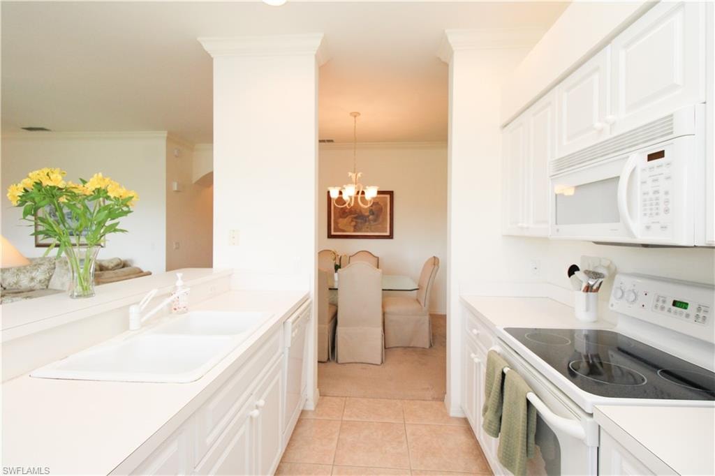 Kitchen featuring white appliances, light tile patterned floors, an inviting chandelier, sink, and white cabinets