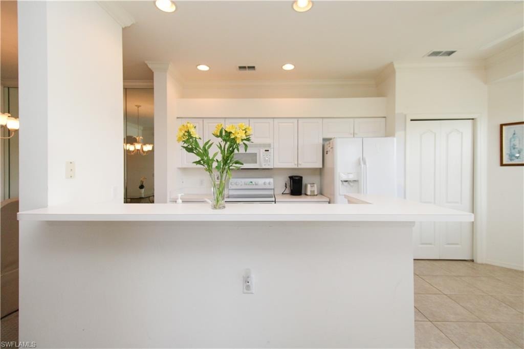 Kitchen with white cabinets, white appliances, ornamental molding, and light tile patterned flooring