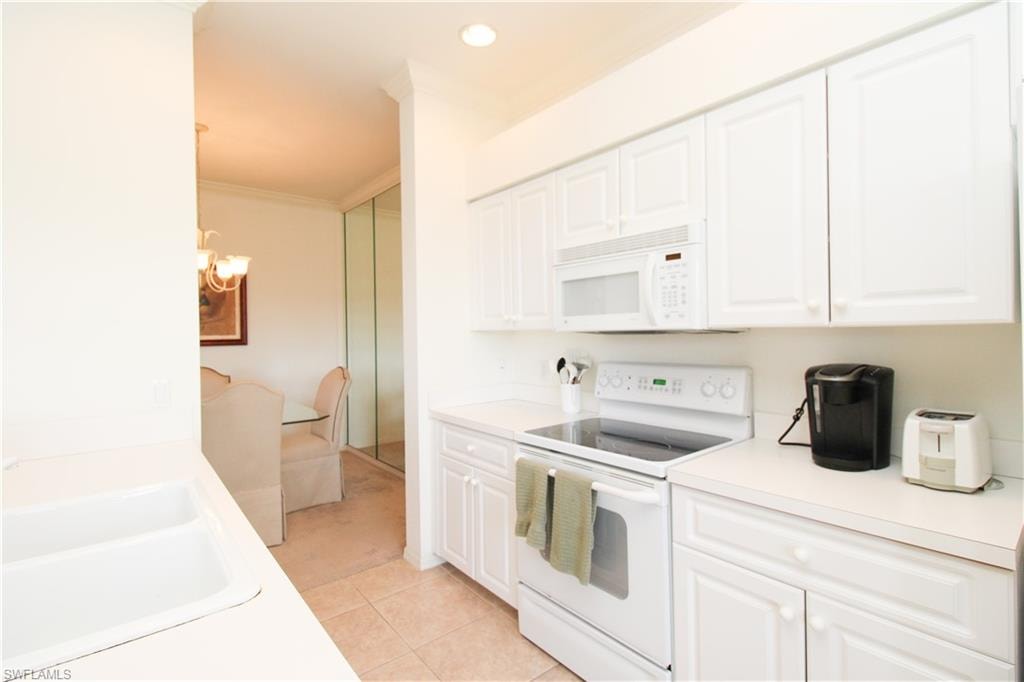Kitchen featuring white cabinets, white appliances, light tile patterned floors, and ornamental molding