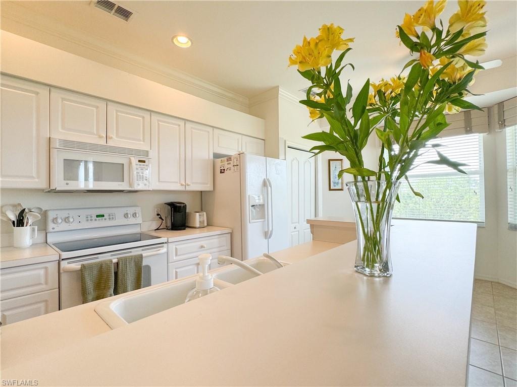 Kitchen with white appliances, light tile patterned floors, crown molding, sink, and white cabinets