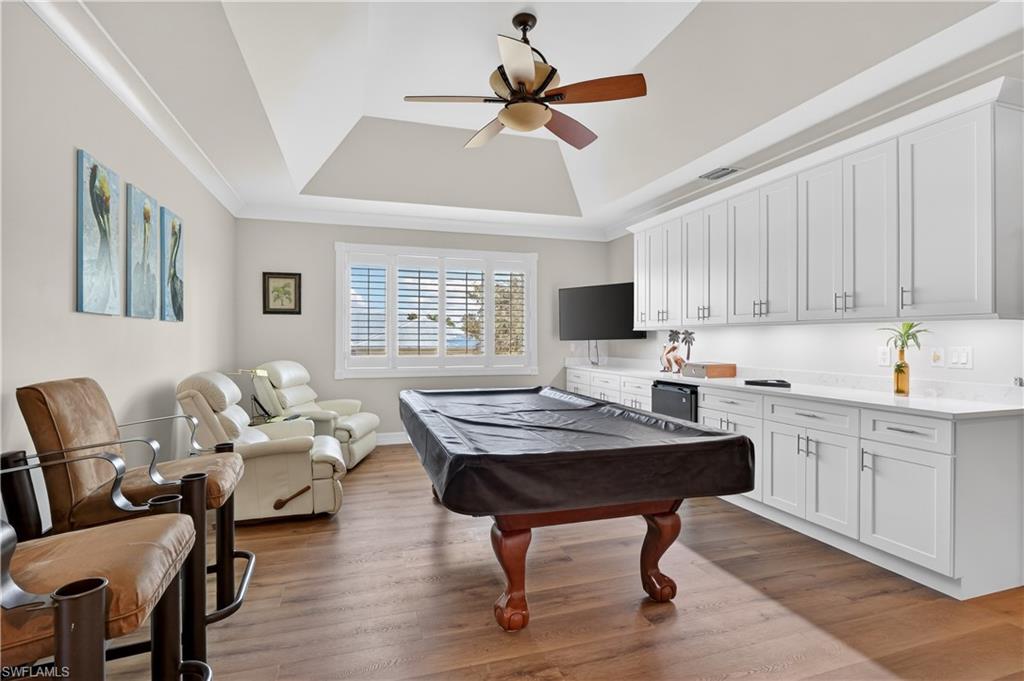 Rec room with light wood-style flooring, a ceiling fan, a tray ceiling, billiards, and crown molding