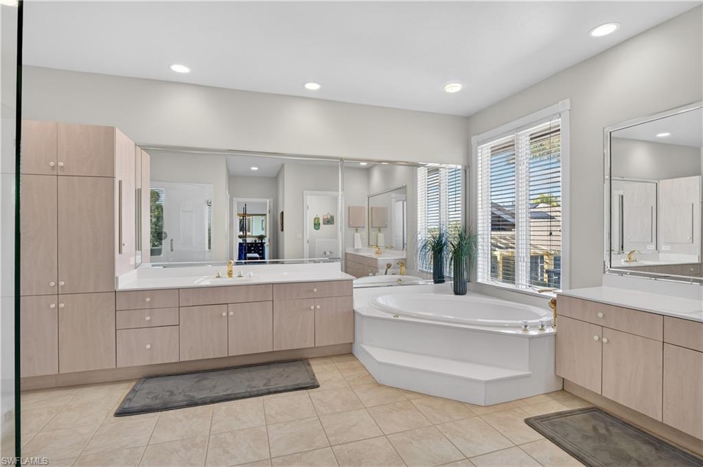 Full bathroom featuring two vanities, a garden tub, light tile patterned floors, and recessed lighting