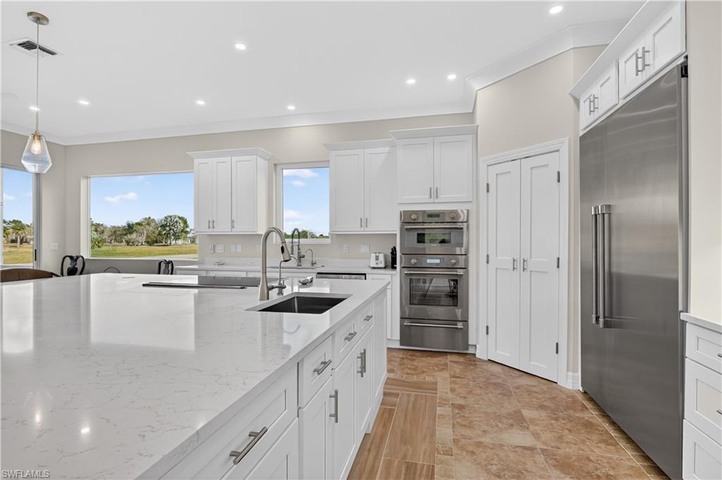 Kitchen with white cabinetry, stainless steel appliances, light stone counters, crown molding, and recessed lighting